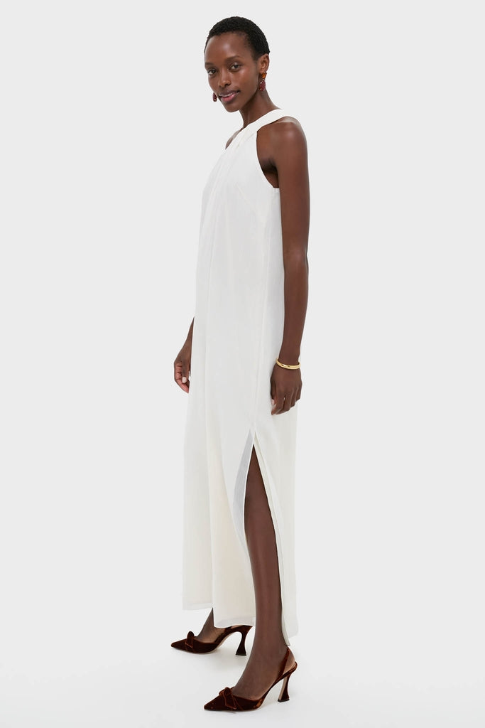 Model in classic Ivory Soleil Gown, featuring a sleeveless design, high neckline, and thigh-high slit. Paired with brown velvet slingback heels and gold accessories for an effortless, high-end look.