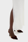 Model wearing classic Ivory Soleil Gown with side slit, elegantly paired with dark brown velvet sling-back heels featuring bows, embodying effortless, high-end style for wedding guests.