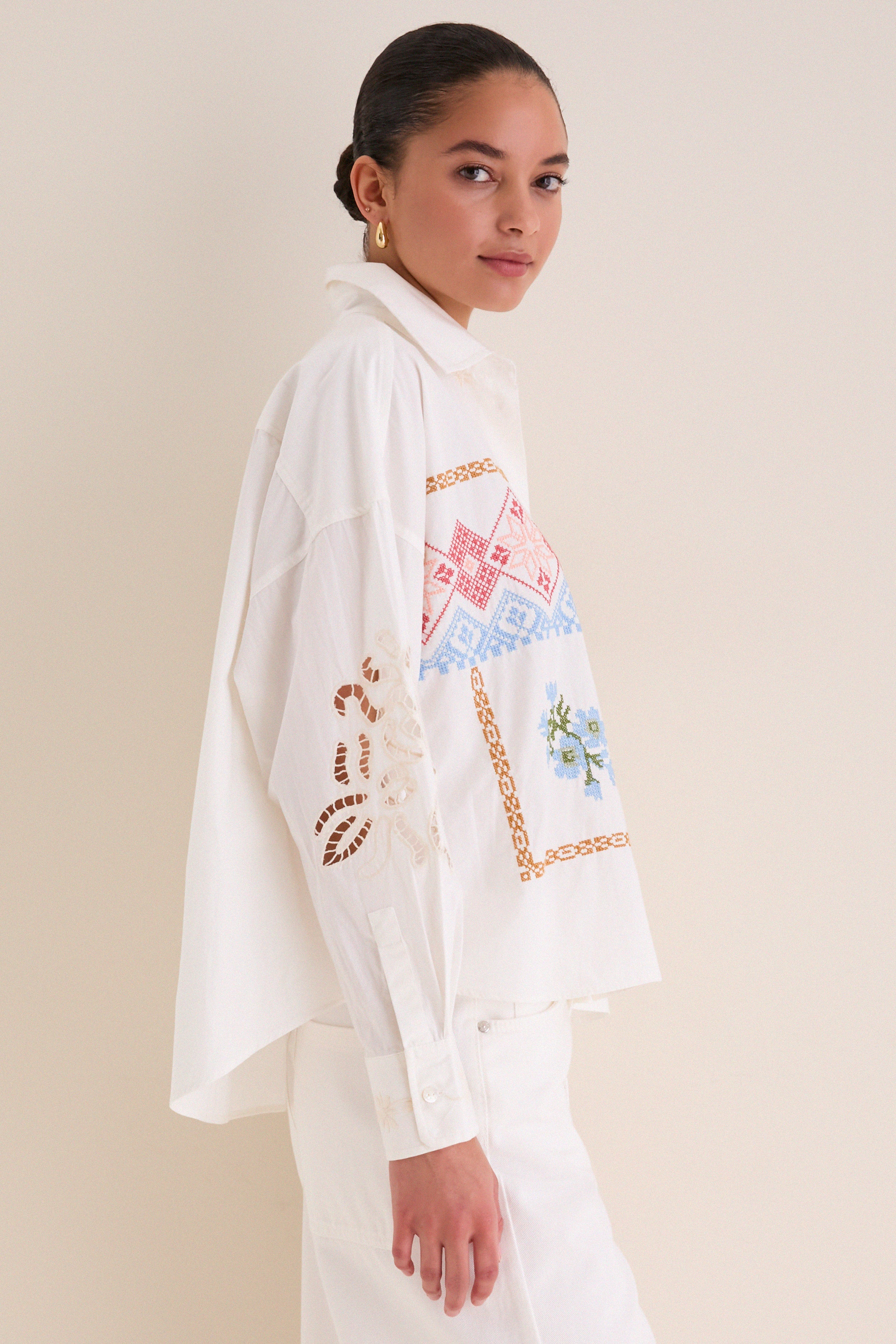 Model in profile wearing the White Fonte Shirt, a classic, effortlessly chic blouse with colorful cross-stitch embroidery and eyelet lace, embodying high-end, fun style.