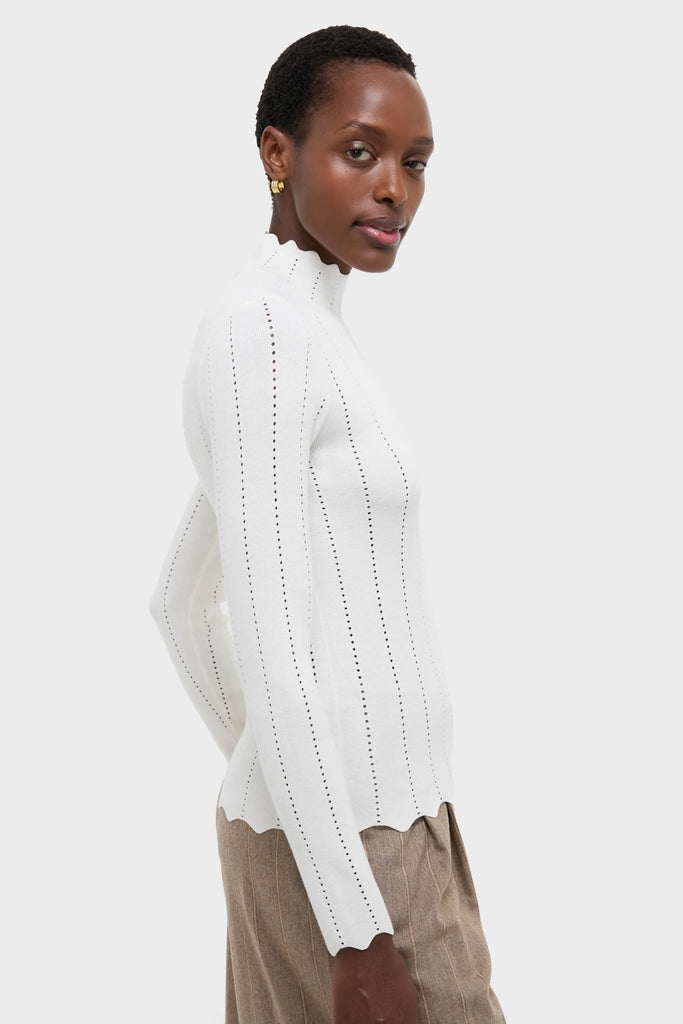 Side-profile of a model in the classic White Pointelle Knit Allen Turtleneck, featuring scalloped edges, paired with pinstriped trousers for an effortless, high-end look.