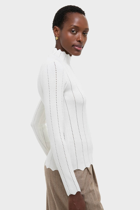 Side-profile of a model in the classic White Pointelle Knit Allen Turtleneck, featuring scalloped edges, paired with pinstriped trousers for an effortless, high-end look.