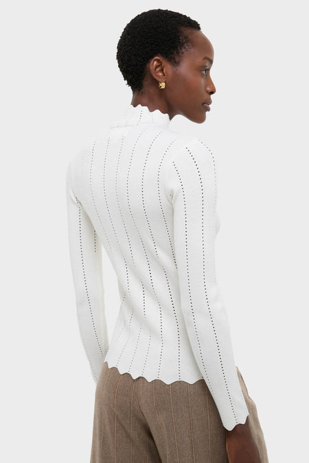 Woman wearing the classic White Pointelle Knit Allen Turtleneck with scalloped edges and a ruffled mock-neck, paired with high-waisted pinstripe trousers for an effortless, high-end look.