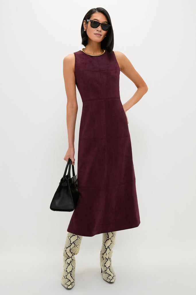 Woman wearing the Winetasting Vegan Suede Manon Dress with classic snakeskin-print boots and gold jewelry, effortlessly holding a black leather tote, embodying high-end, fun style.