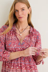 Woman in Americana Batik Stripe Long Sleeve Salty Paloma Caftan with floral print, adjusting ties; paired with blue beads and gold hoops, embodying effortless bohemian elegance.