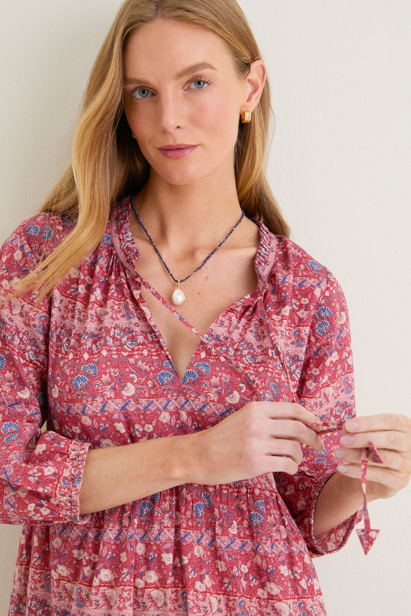 Woman in Americana Batik Stripe Long Sleeve Salty Paloma Caftan with floral print, adjusting ties; paired with blue beads and gold hoops, embodying effortless bohemian elegance.