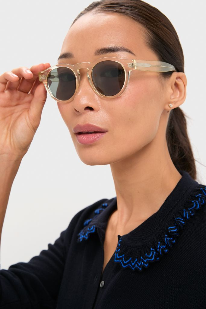 Woman holding Champagne Leonard Sunglasses, featuring classic round lenses and translucent frames, embodying effortless style and high-end craftsmanship. Perfect for everyday fun and versatility.