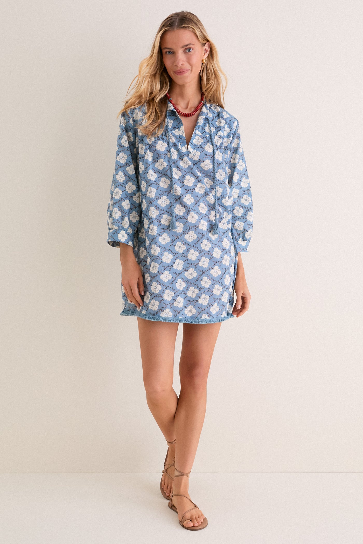 Woman models the Bloom Lagoon Bondi Coverup; an effortless, boho-chic mini dress with tassel neckties, fringed hem, and intricate embroidery, styled with sandals and accessories.