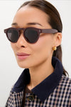 A person wearing Bordeaux Leonard Sunglasses with matte brown frames, embodying a classic and effortless style, paired with gold hoops and a gingham jacket.