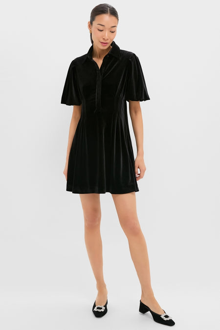 Woman in Black Velvet Mini Delaney Dress with classic polo collar, flutter sleeves, and rhinestone-buckled mules, exuding effortless, high-end style for fun, versatile occasions.