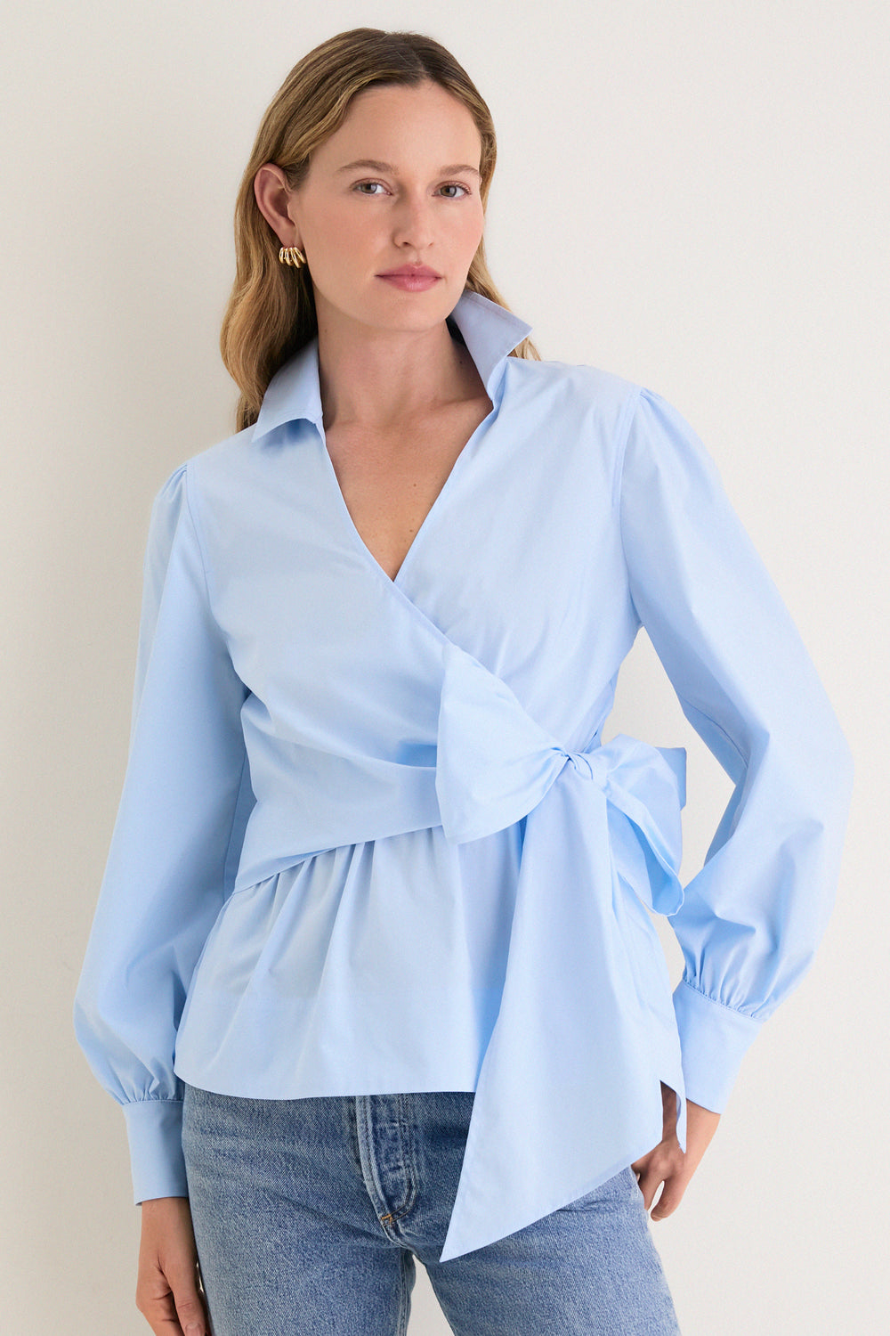 Female model in a classic, effortless French Blue Tie Front Bow Bea Blouse, showcasing its chic wrap design, peplum waist, and elegant self-tie bow.