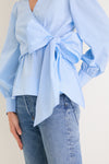 French Blue Tie Front Bow Bea Blouse with classic wrap design, effortless peplum waist, and fun oversized bow, paired stylishly with medium-wash jeans for a high-end look.