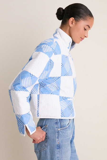 Young woman in a classic, high-end Blue and White Quilted Cropped Townley Jacket, showcasing effortless style with patchwork design, styled with high-waisted denim for a fun, confident look.