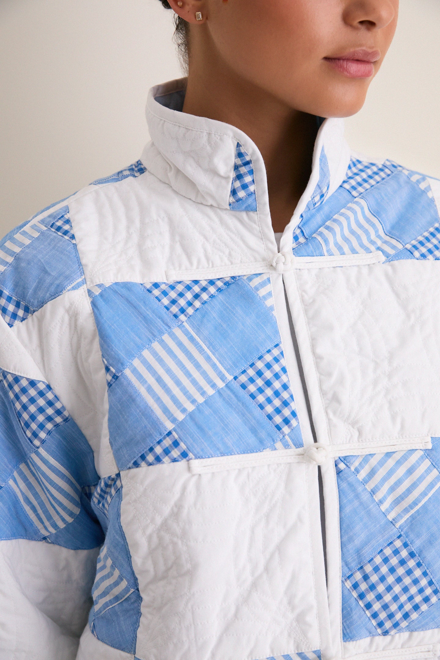 Close-up of the Blue and White Quilted Cropped Townley Jacket, showcasing its classic patchwork design with stand collar and frog closures, offering an effortless, high-end style.