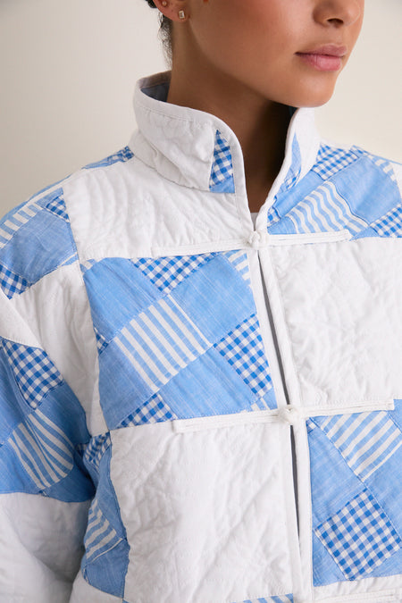 Close-up of the Blue and White Quilted Cropped Townley Jacket, showcasing its classic patchwork design with stand collar and frog closures, offering an effortless, high-end style.