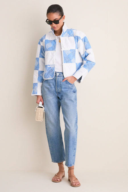 Person stylishly dons the Blue and White Quilted Cropped Townley Jacket, pairing it with light-wash jeans and chic accessories for an effortless, high-end look.