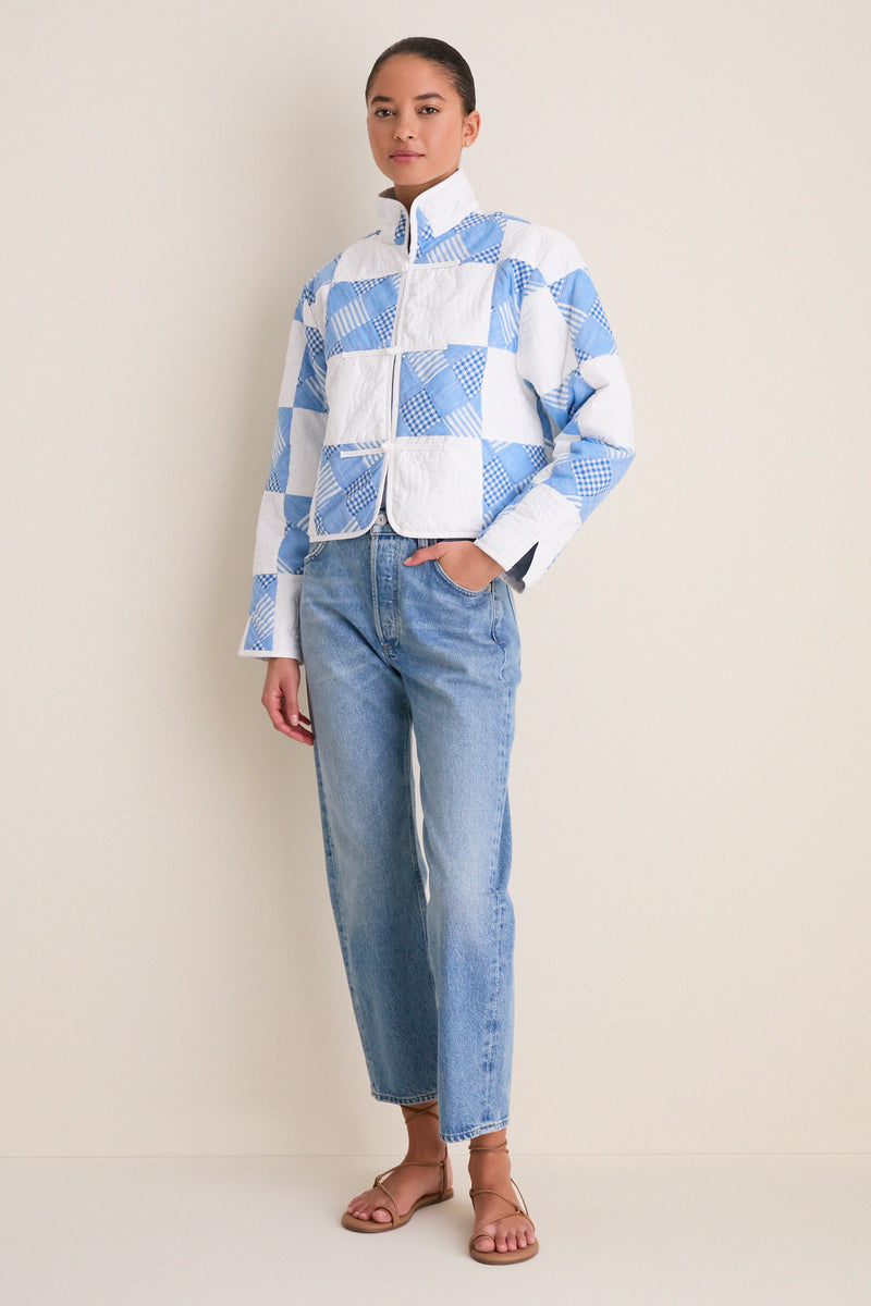 Model wearing the Blue and White Quilted Cropped Townley Jacket with a classic patchwork design, effortlessly styled with light-wash jeans and tan sandals for a high-end, fun look.