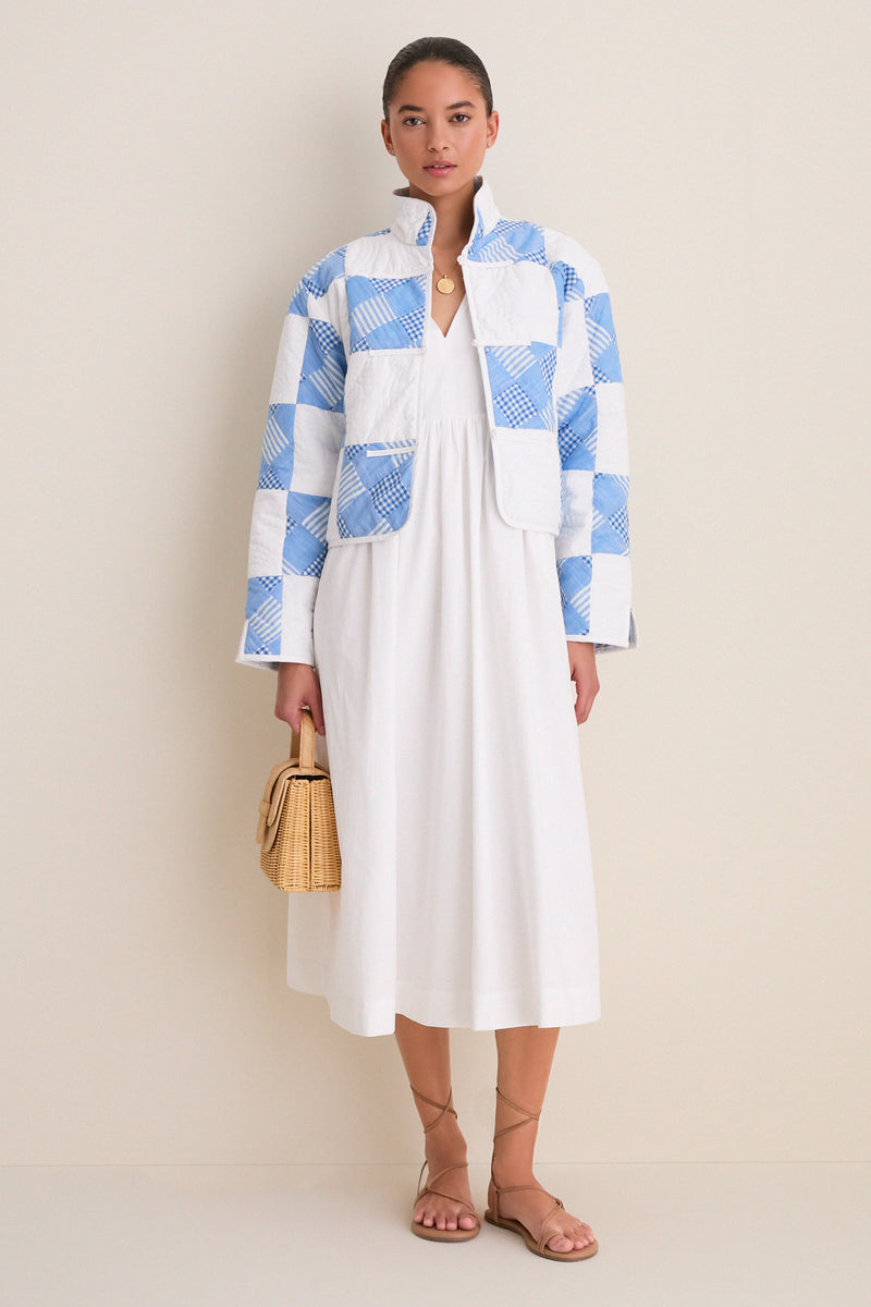 Woman wearing the Blue and White Quilted Cropped Townley Jacket, a classic, high-end layer with patchwork checks, styled effortlessly over a white dress, holding a woven handbag.