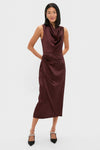 Woman models the Chocolate Satin Sinclair Dress, a classic, high-end burgundy midi with a cowl neck and tulip-style skirt, styled effortlessly with sparkly slingback heels.