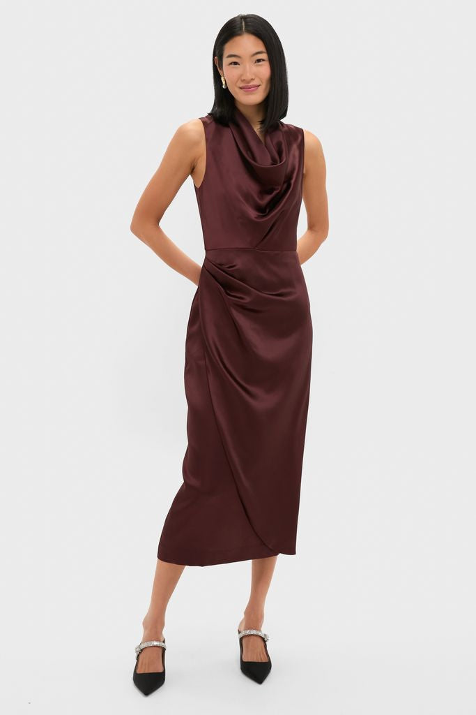 Woman models the Chocolate Satin Sinclair Dress, a classic, high-end burgundy midi with a cowl neck and tulip-style skirt, styled effortlessly with sparkly slingback heels.