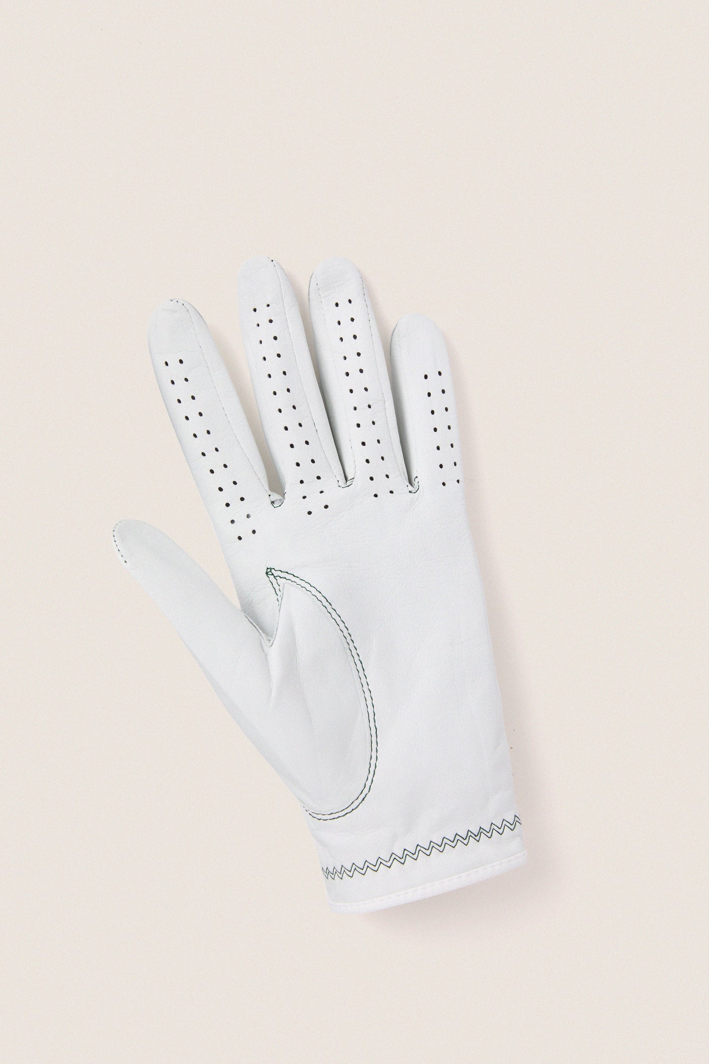 White Left Hand Golf Glove featuring classic leather design, effortless ventilation perforations, and fun zig-zag wrist stitching, embodying high-end comfort and flexibility for an exciting golf experience.
