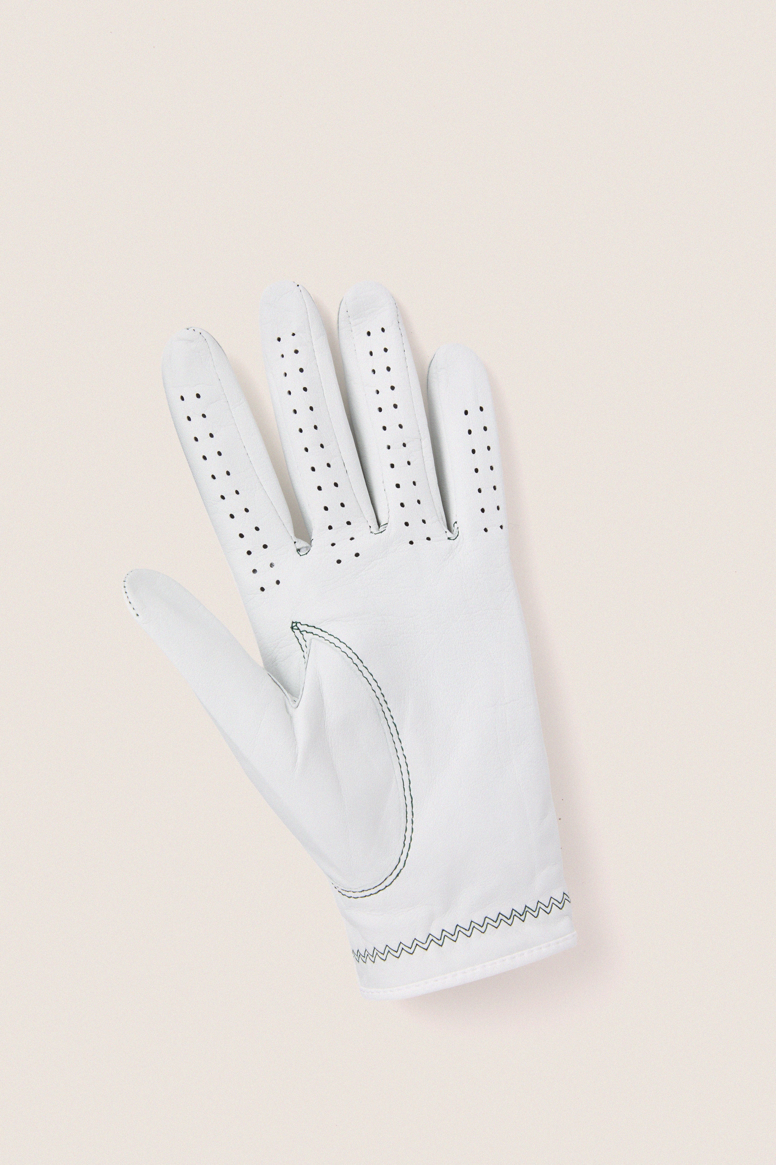 White Left Hand Golf Glove featuring classic leather design, effortless ventilation perforations, and fun zig-zag wrist stitching, embodying high-end comfort and flexibility for an exciting golf experience.