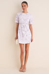 Woman in Lilac Floral Crystal Embellished Floria Mini Dress, clutch and sandals, exuding classic, effortless elegance and fun for elevated daytime events.