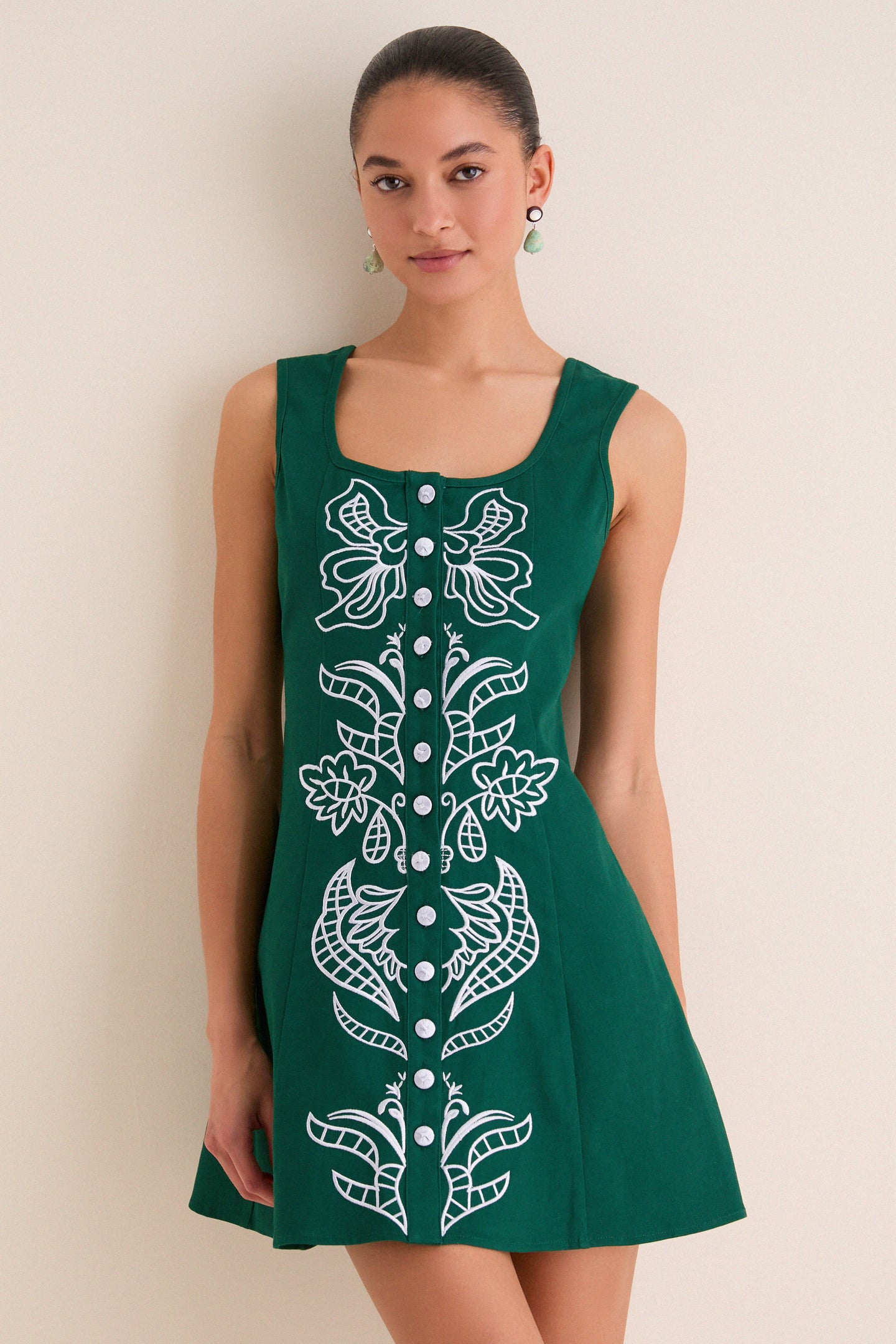 Young woman in a sleeveless, forest-green A-line dress with silver-tone buttons and white embroidery, embodying classic, effortless style and high-end fun.