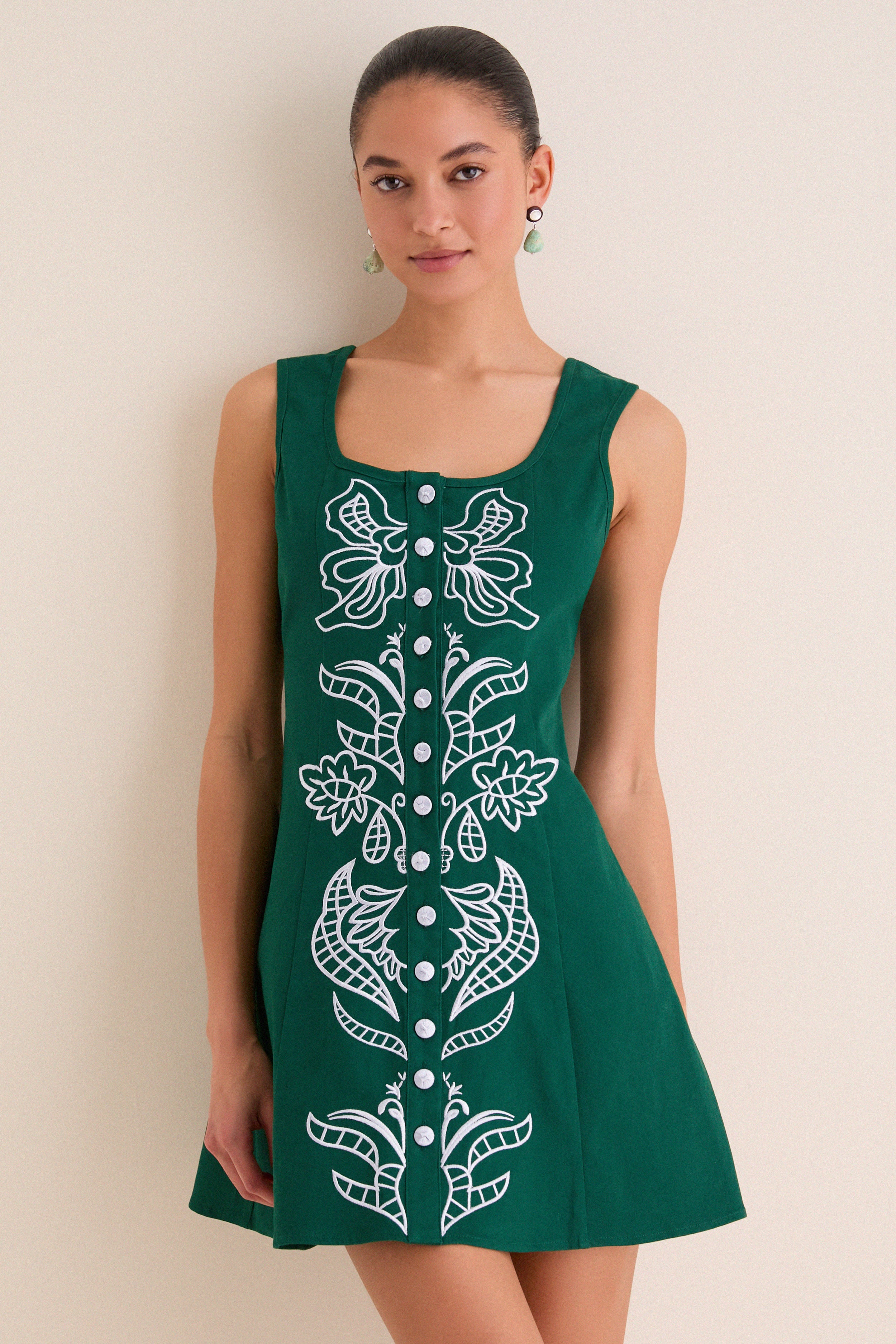 Young woman in a sleeveless, forest-green A-line dress with silver-tone buttons and white embroidery, embodying classic, effortless style and high-end fun.