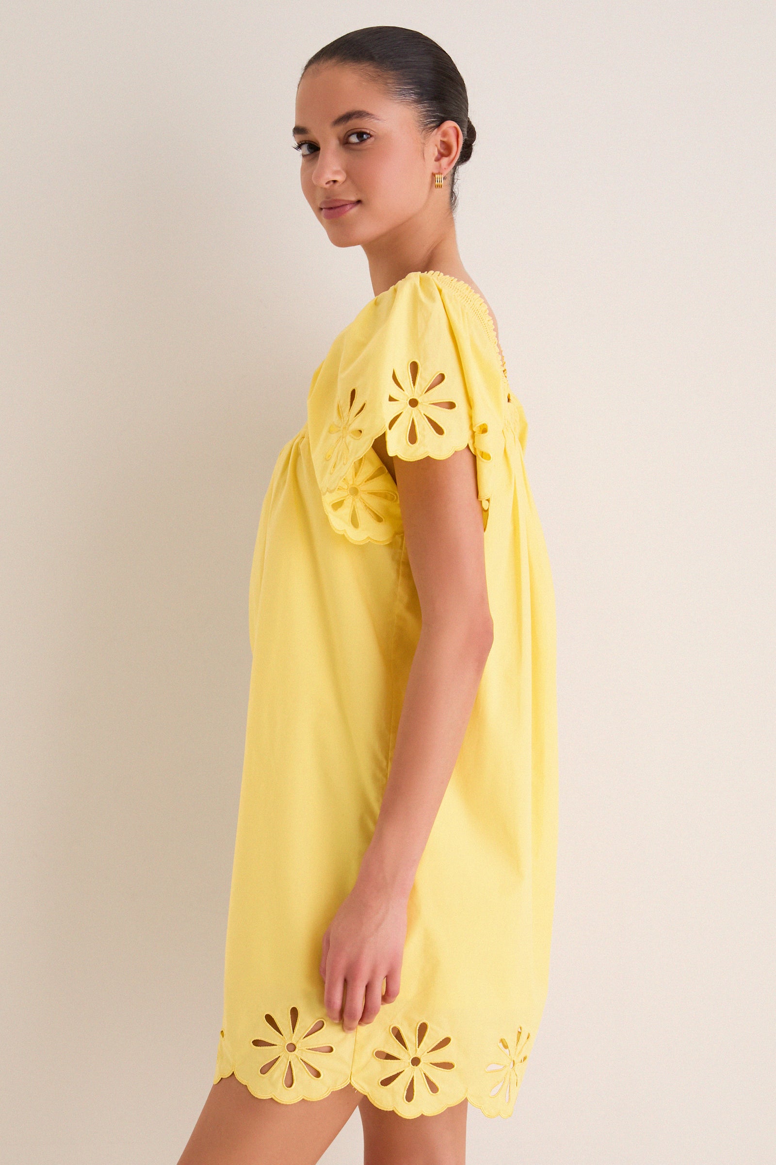 Young woman in profile wearing the Yellow Floral Eyelet Daisy Mini Dress with scalloped edges and daisy eyelet cutouts, embodying classic, effortless, high-end style.