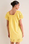 Woman in a classic, sunshine-yellow mini dress with smocked back, puffed sleeves, and eyelet scalloped hem, embodying effortless, high-end style and fun charm.