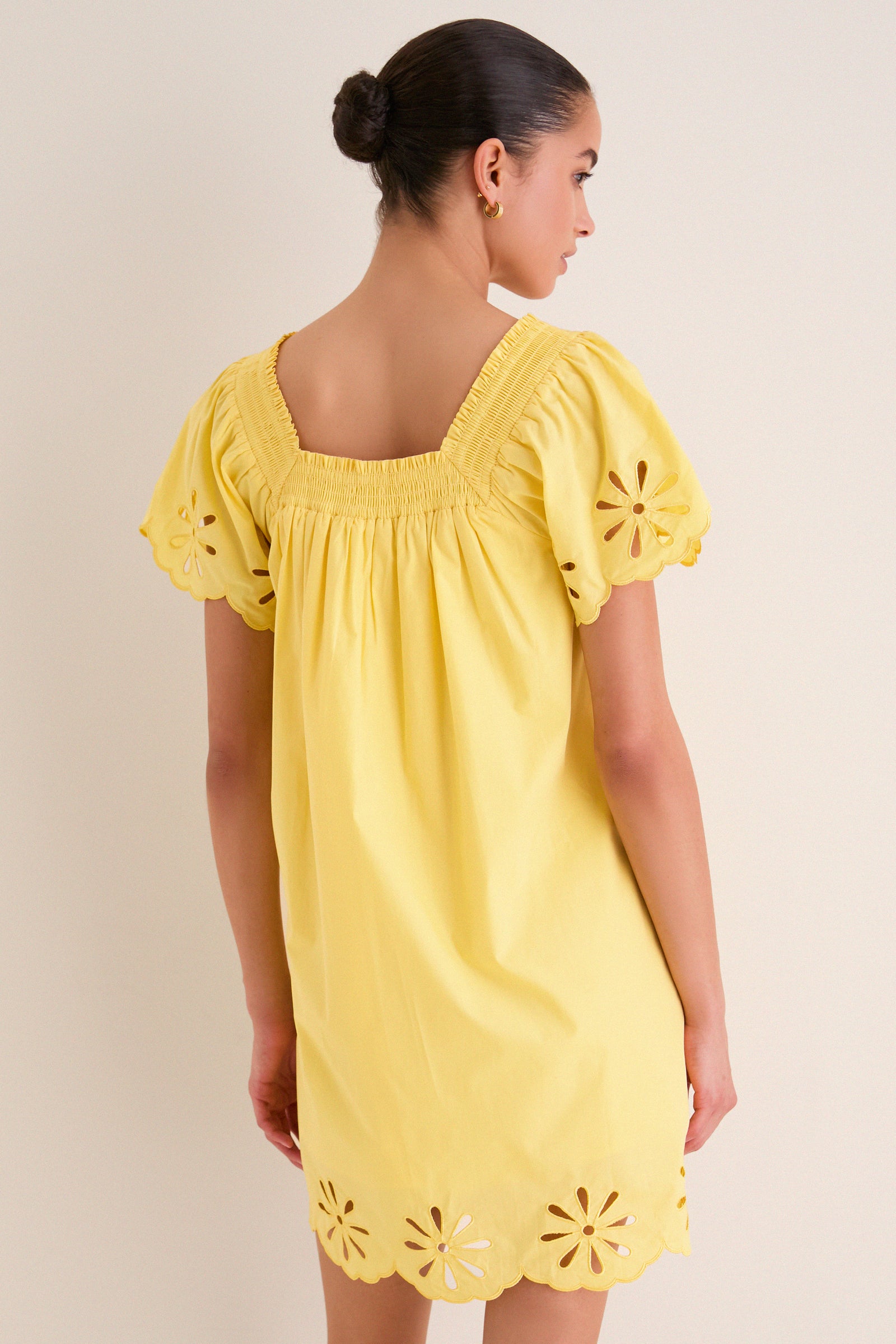 Woman in a classic, sunshine-yellow mini dress with smocked back, puffed sleeves, and eyelet scalloped hem, embodying effortless, high-end style and fun charm.