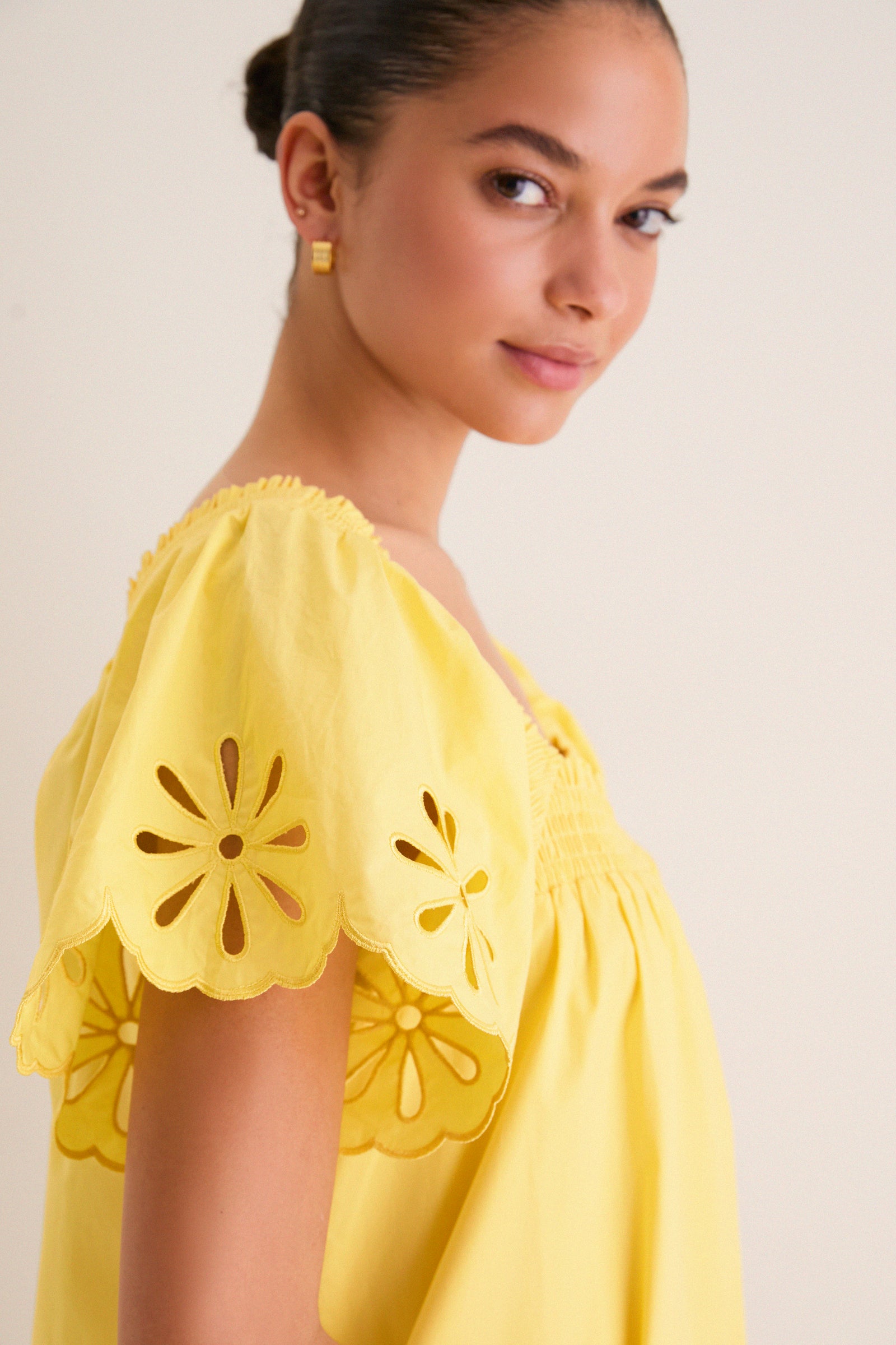 Young woman in a classic, bright yellow mini dress with scalloped flutter sleeves and daisy cutouts, embodying effortless charm and fun. Ideal for high-end, sunny occasions.