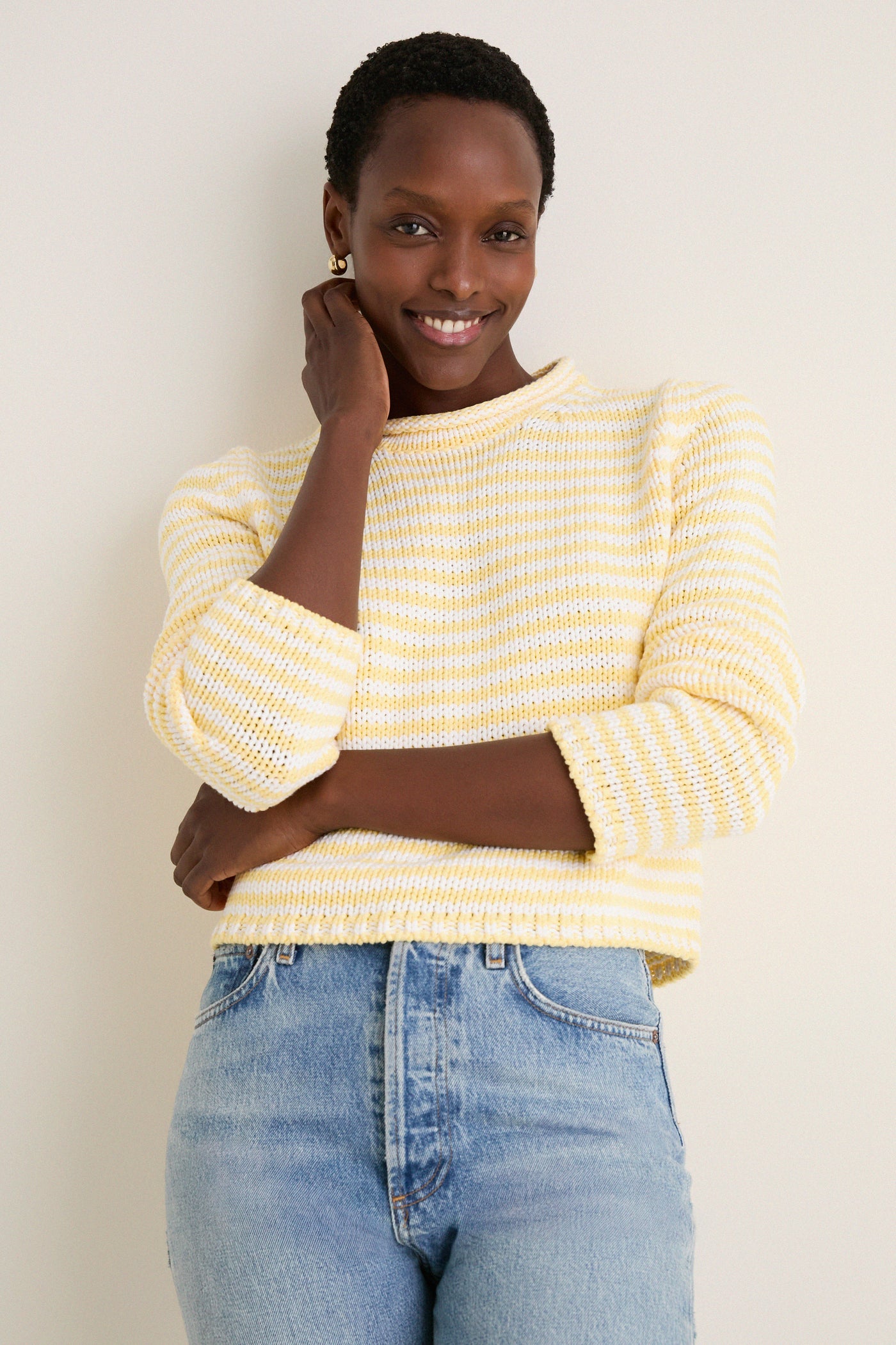 Woman in a Sunshine and Cream Fine Stripe Mini Marina Sweater, showcasing a classic, effortless style with its cozy roll-neck and slim sleeves, embodying fun, high-end fashion.