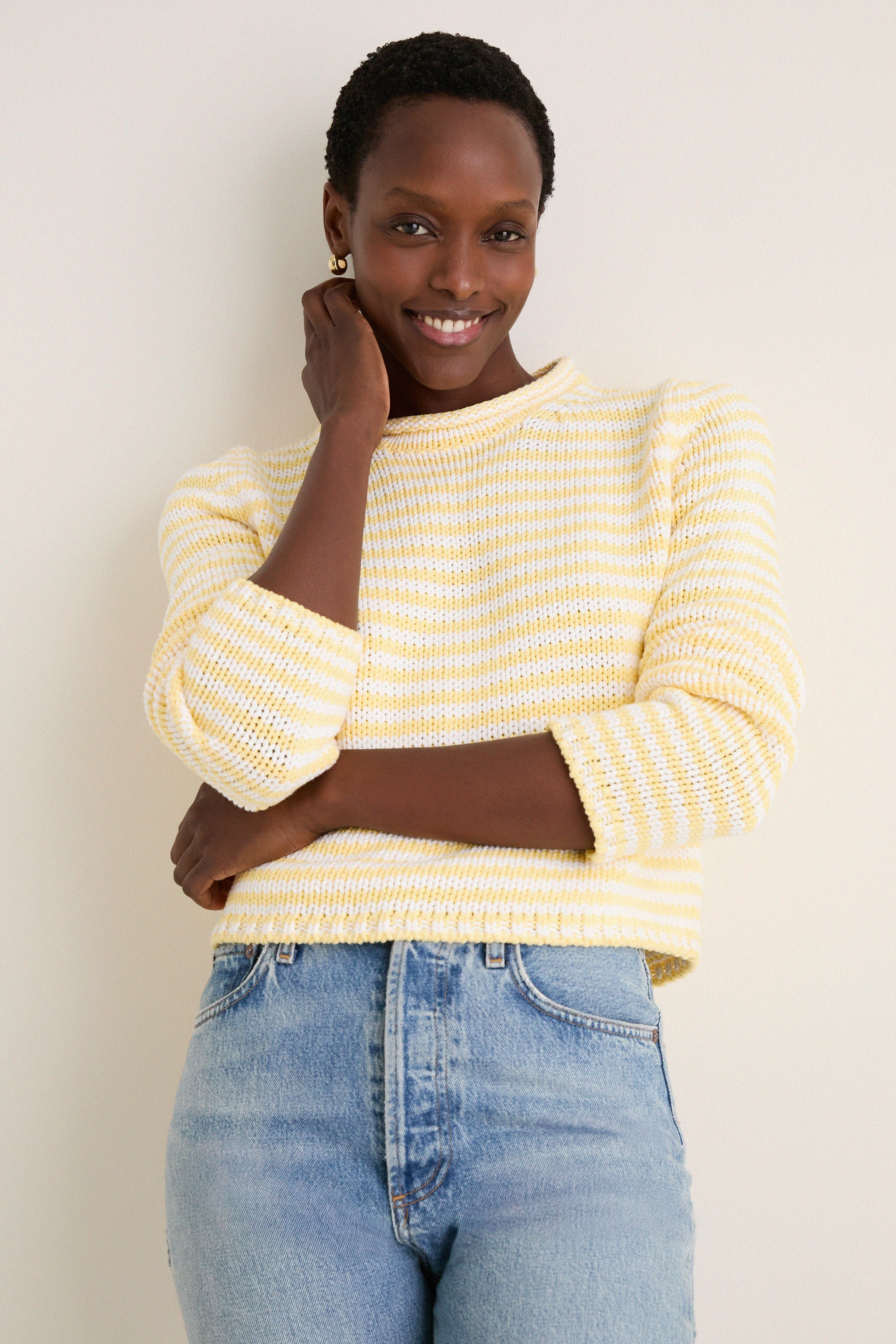 Woman in a Sunshine and Cream Fine Stripe Mini Marina Sweater, showcasing a classic, effortless style with its cozy roll-neck and slim sleeves, embodying fun, high-end fashion.
