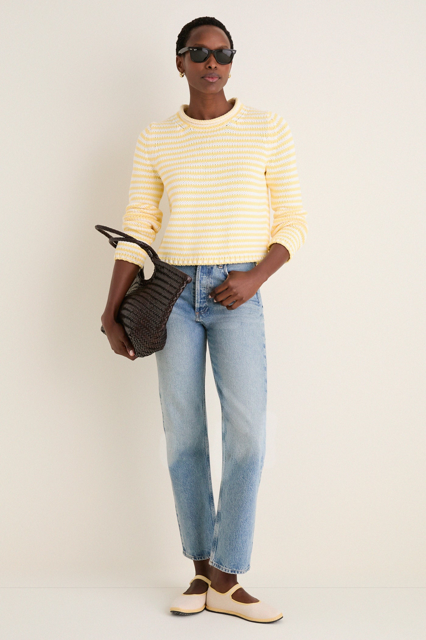 A person wearing the Sunshine and Cream Fine Stripe Mini Marina Sweater with light jeans and chic accessories, embodying a classic, effortless, high-end, and fun spring look.