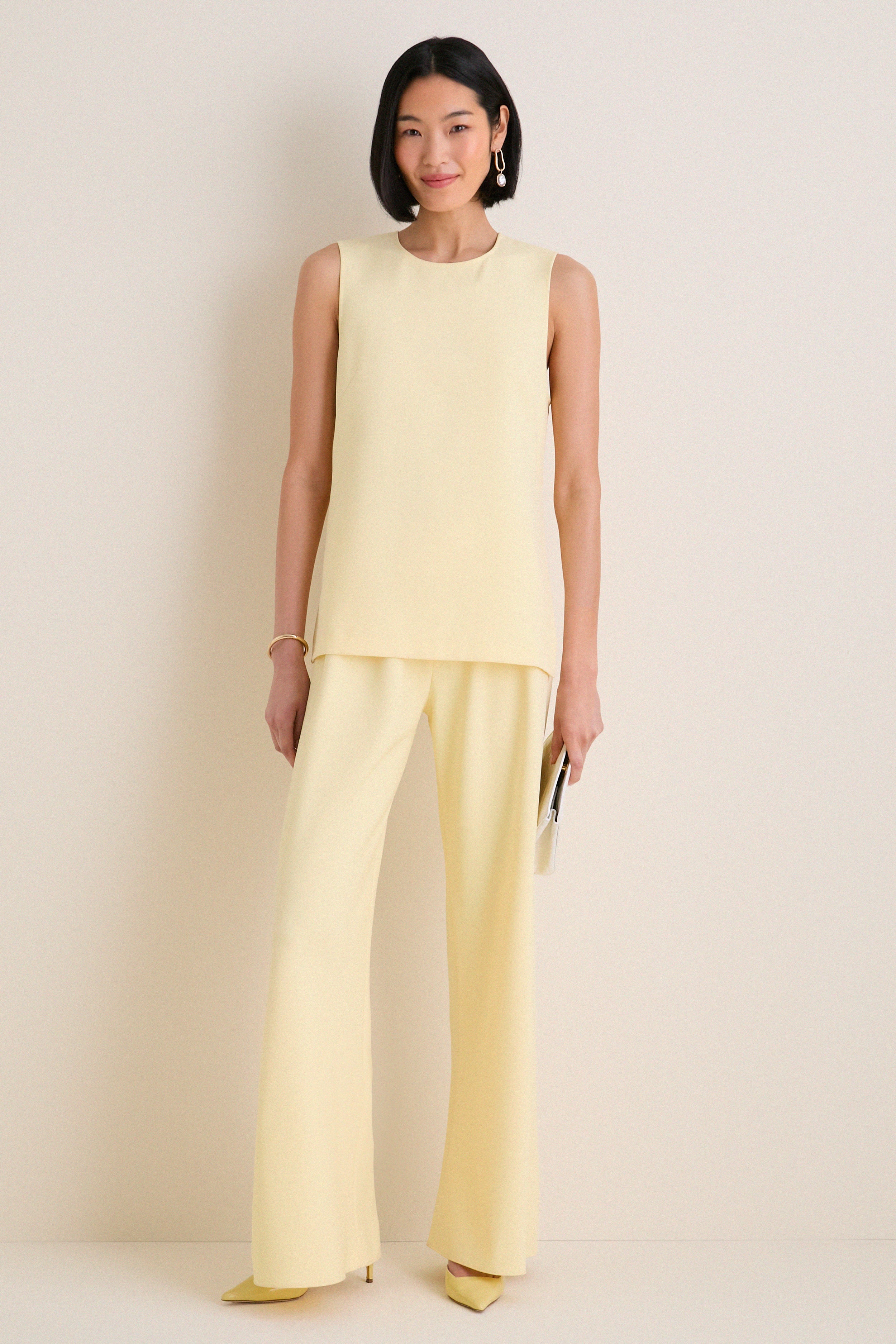 Woman models the Butter Maxime Top, a classic sleeveless tunic with side slits, epitomizing effortless, high-end style, paired with matching trousers and pointed heels.