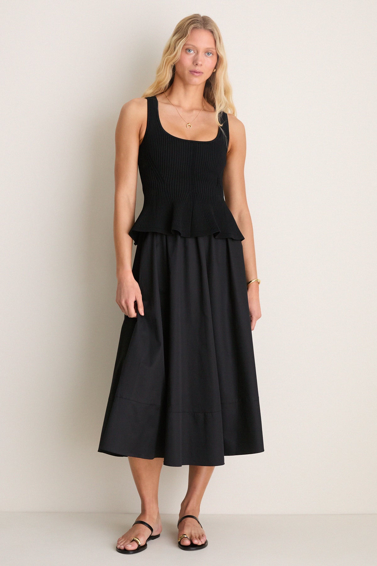 Model in Black Peplum Cara Dress: a classic, mixed-media midi with peplum hem, sleeveless bodice, and A-line skirt, embodying an effortless, high-end style.