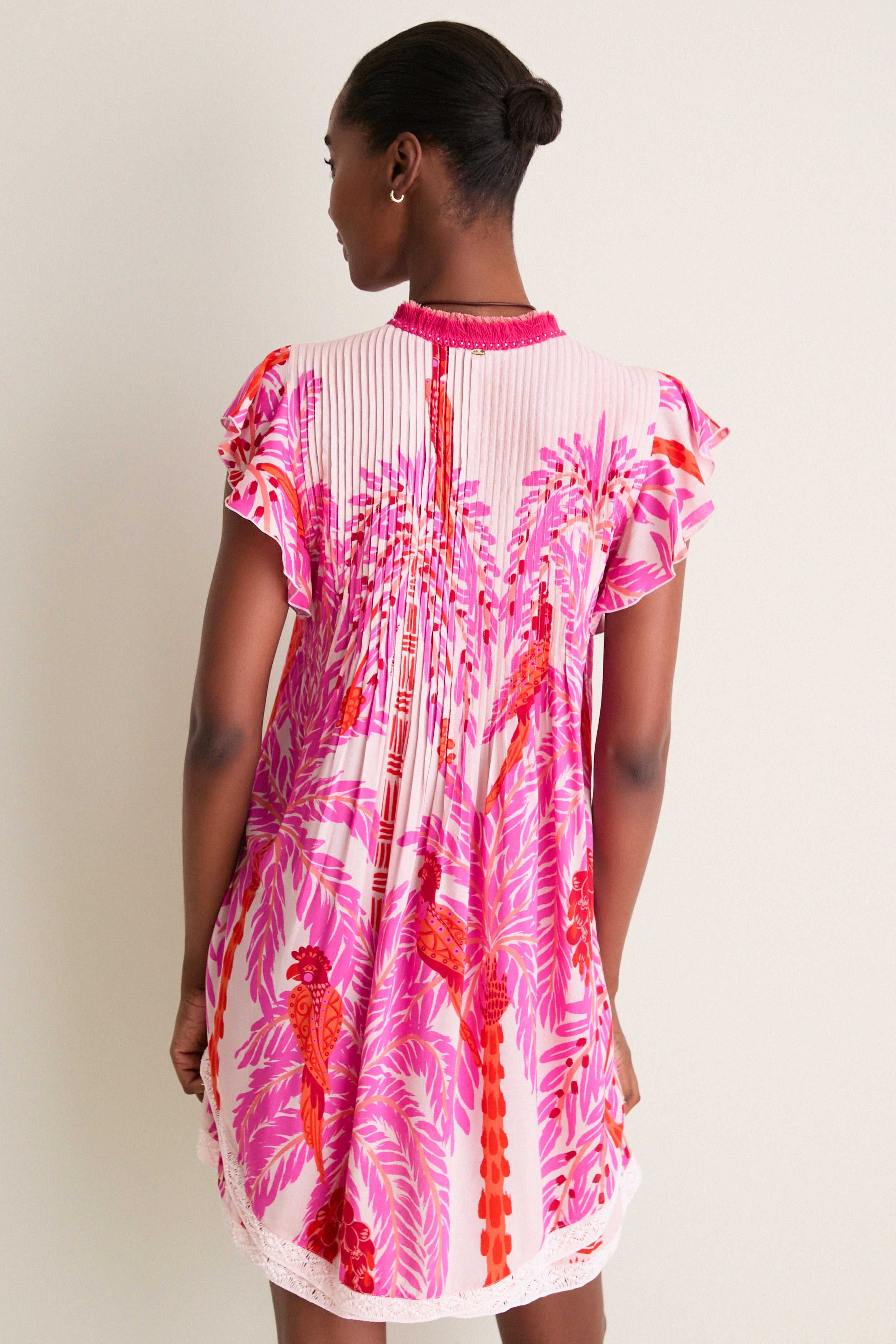 Back view of a woman in the Pink Holy Snake Mini Sasha Dress, featuring a classic, fun, tropical print with flutter sleeves, exuding effortless, high-end boho-chic style.