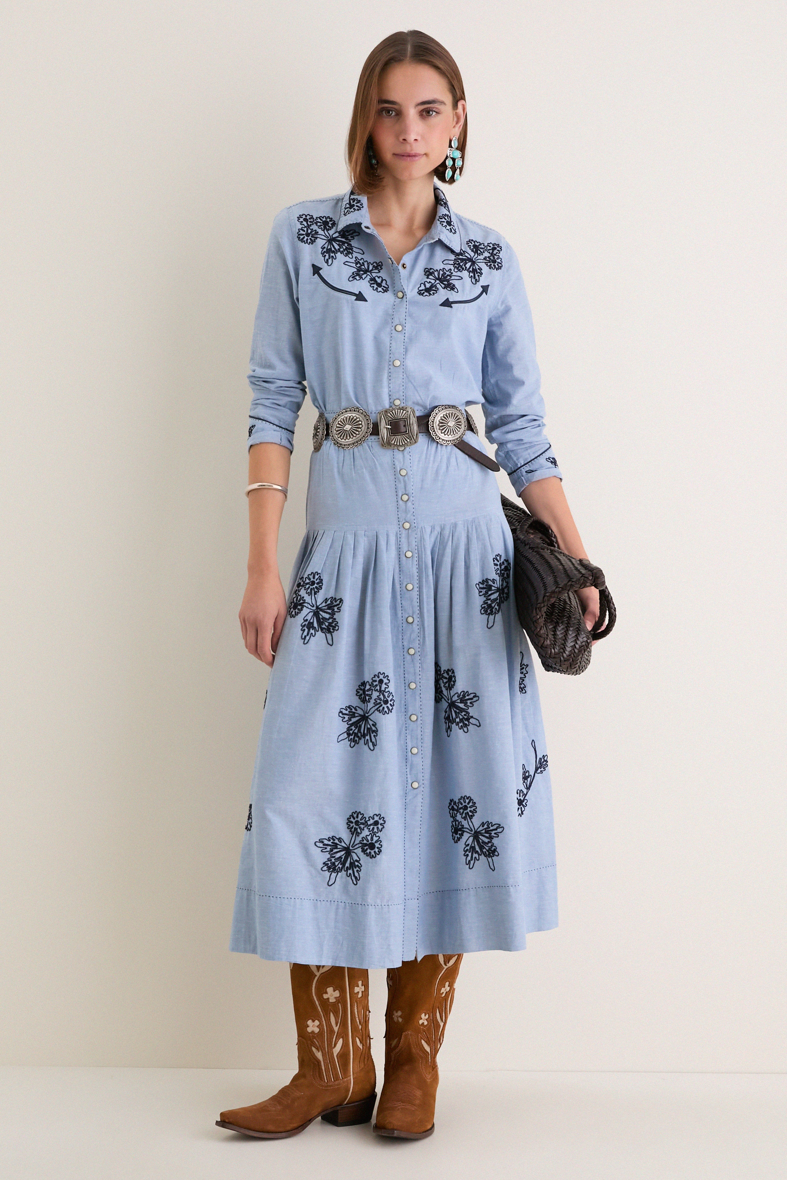 Woman in The Chambray Embroidered Western Shirt with floral embroidery, styled with a silver concho belt and cowboy boots, embodying classic, effortless, high-end fashion.