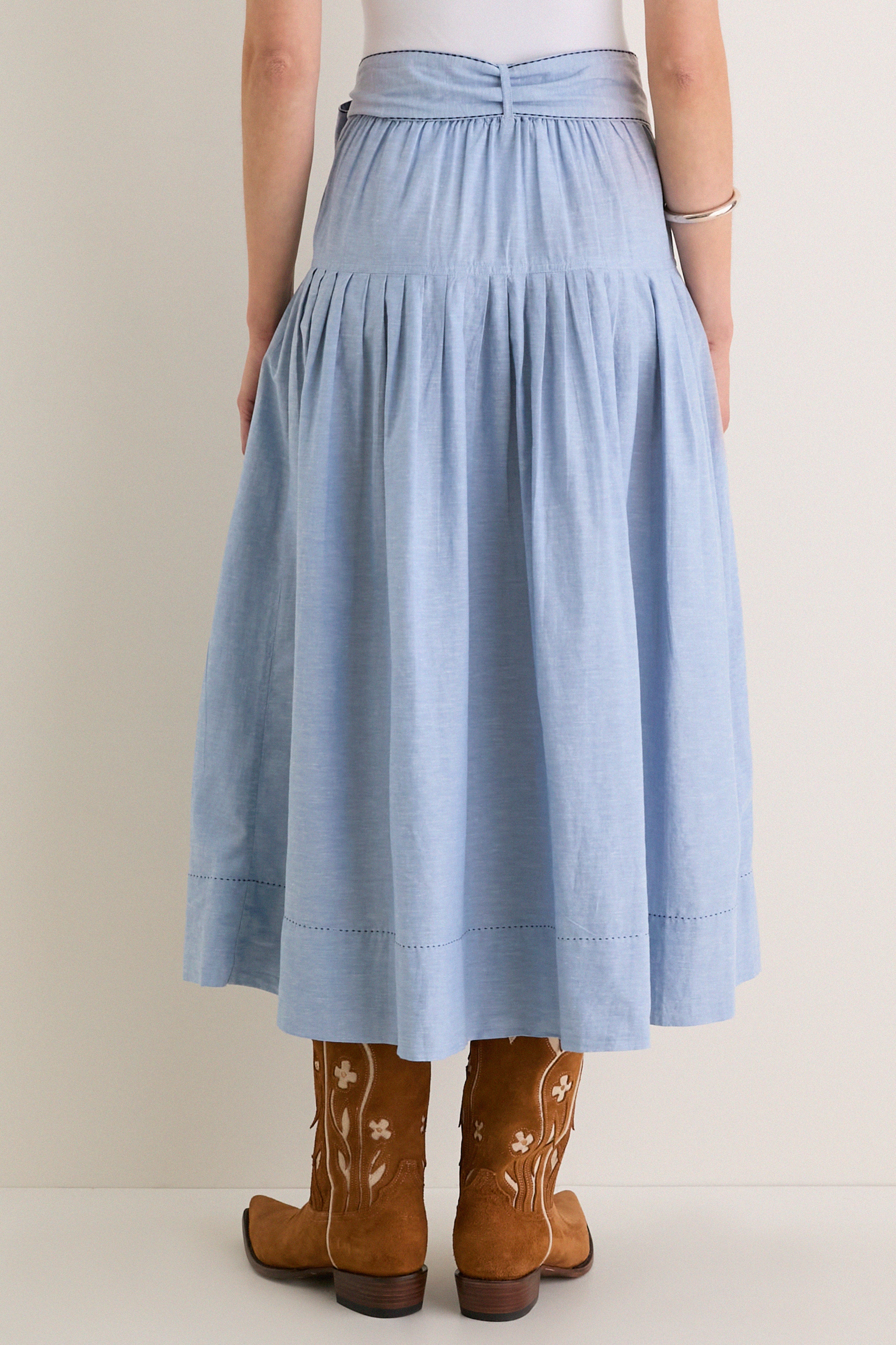 The Chambray Embroidered Highland Skirt paired with cowboy boots exudes classic, effortless style, blending fun western inspiration with high-end, refined details like gentle pleats and floral embroidery.