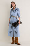 Woman wearing The Chambray Embroidered Highland Skirt with navy floral embroidery, paired with a silver concho belt, turquoise earrings, and cowboy boots for a classic, effortless look.