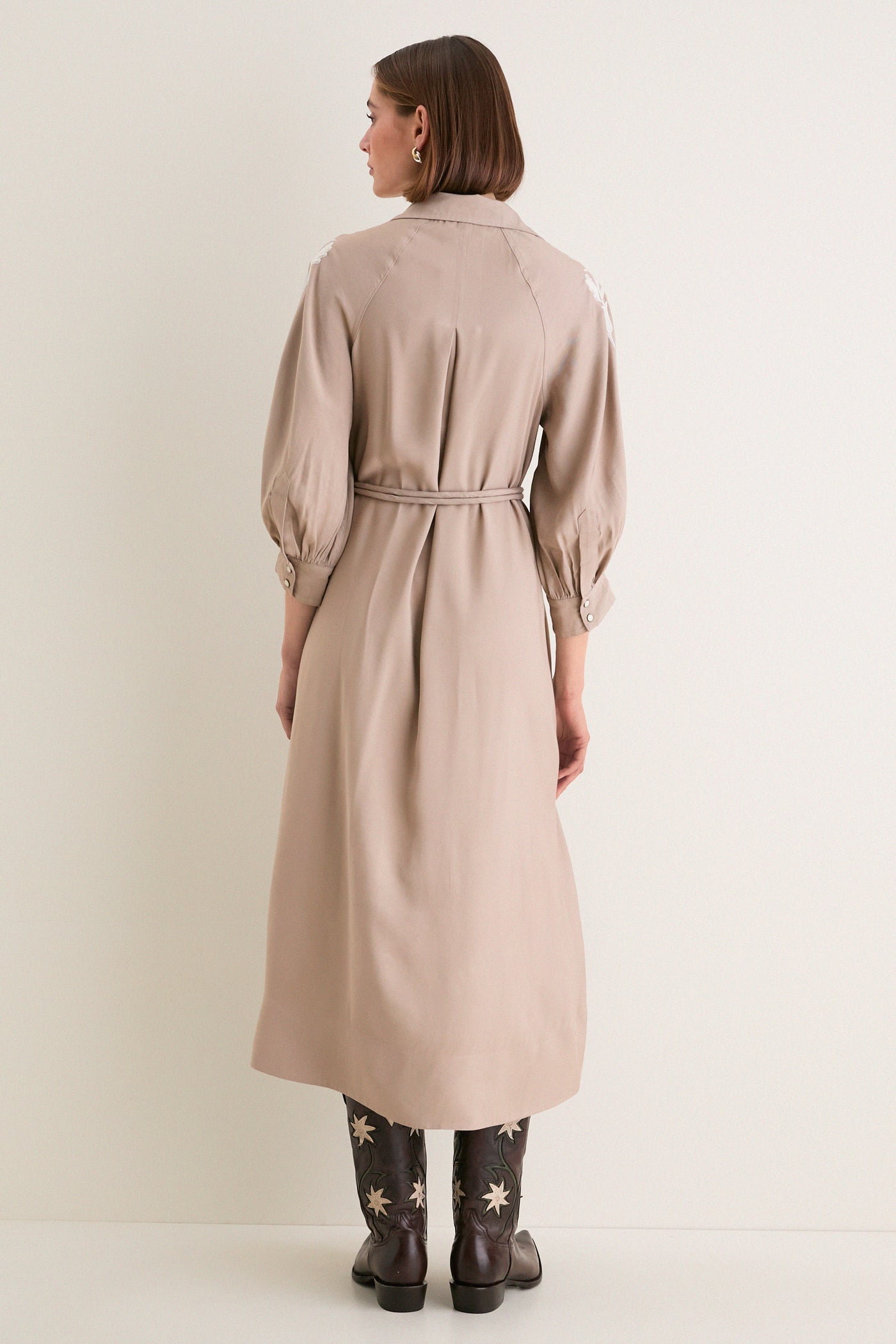 Woman in a classic Soft Tan Western Embroidered Herd Dress with a belted waist and billowed sleeves, paired with star-embroidered cowboy boots, radiating effortless, high-end style.