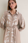 Young woman models the Soft Tan Western Embroidered Herd Dress with classic, effortless charm; featuring billowy sleeves, botanical embroidery, and a knotted waist belt for a high-end look.