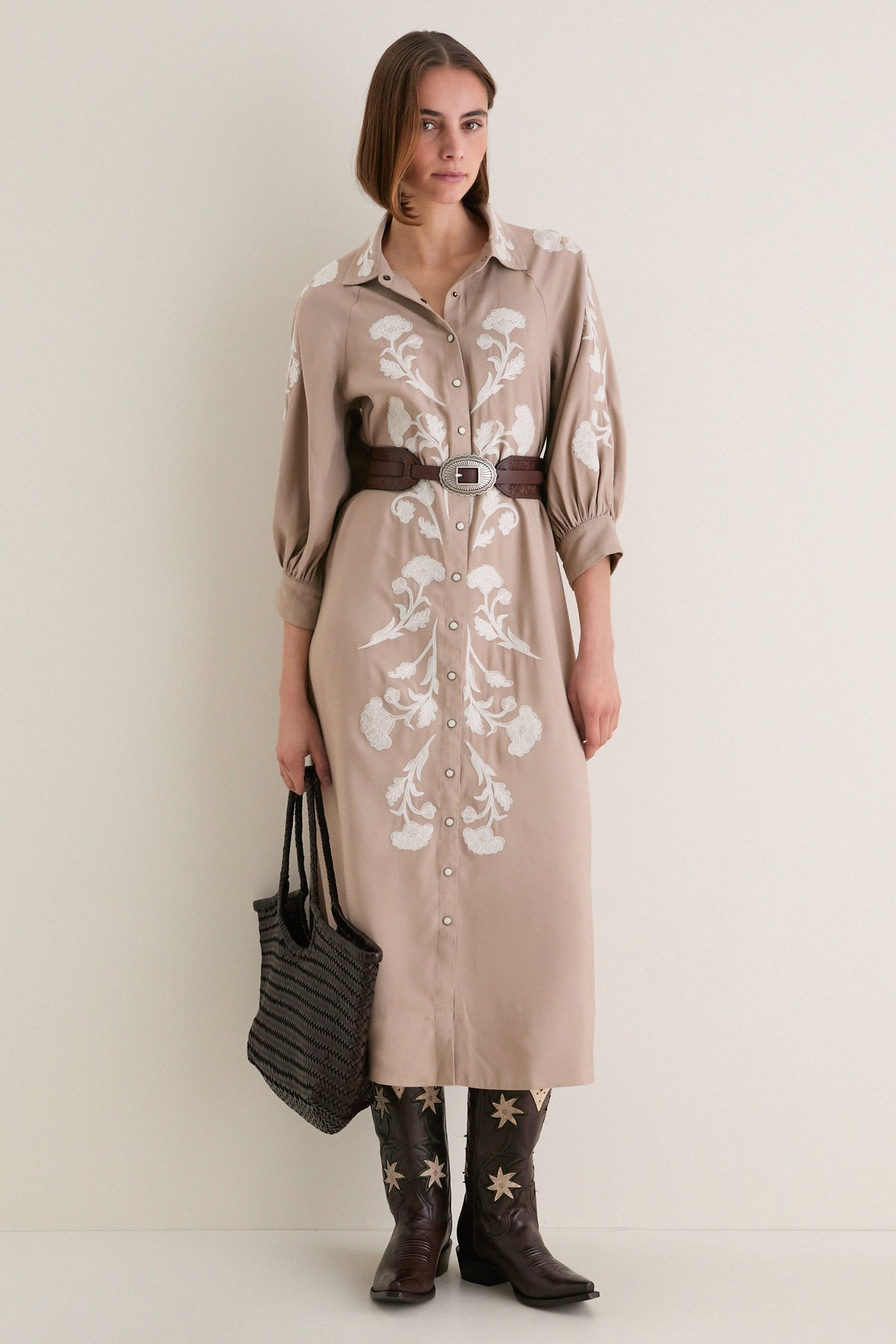 Model wearing the Soft Tan Western Embroidered Herd Dress, a classic shirtdress with floral embroidery, cinched waist, and cowboy boots, exuding effortless, high-end style.
