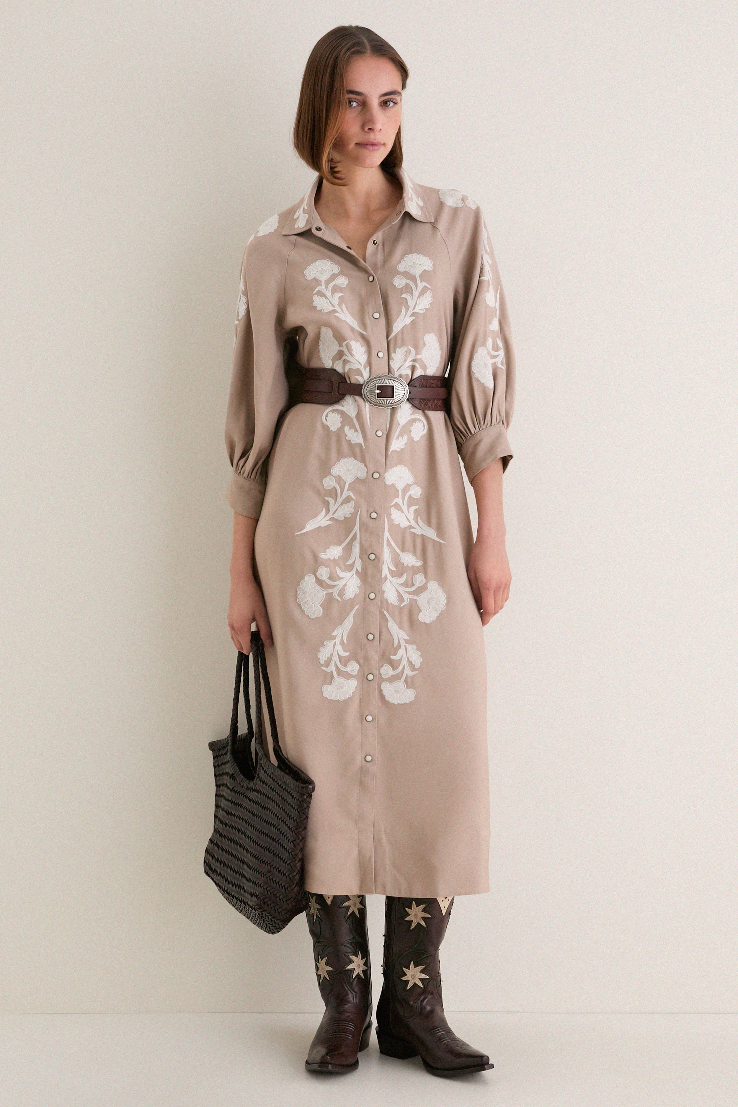 Model wearing the Soft Tan Western Embroidered Herd Dress, a classic shirtdress with floral embroidery, cinched waist, and cowboy boots, exuding effortless, high-end style.