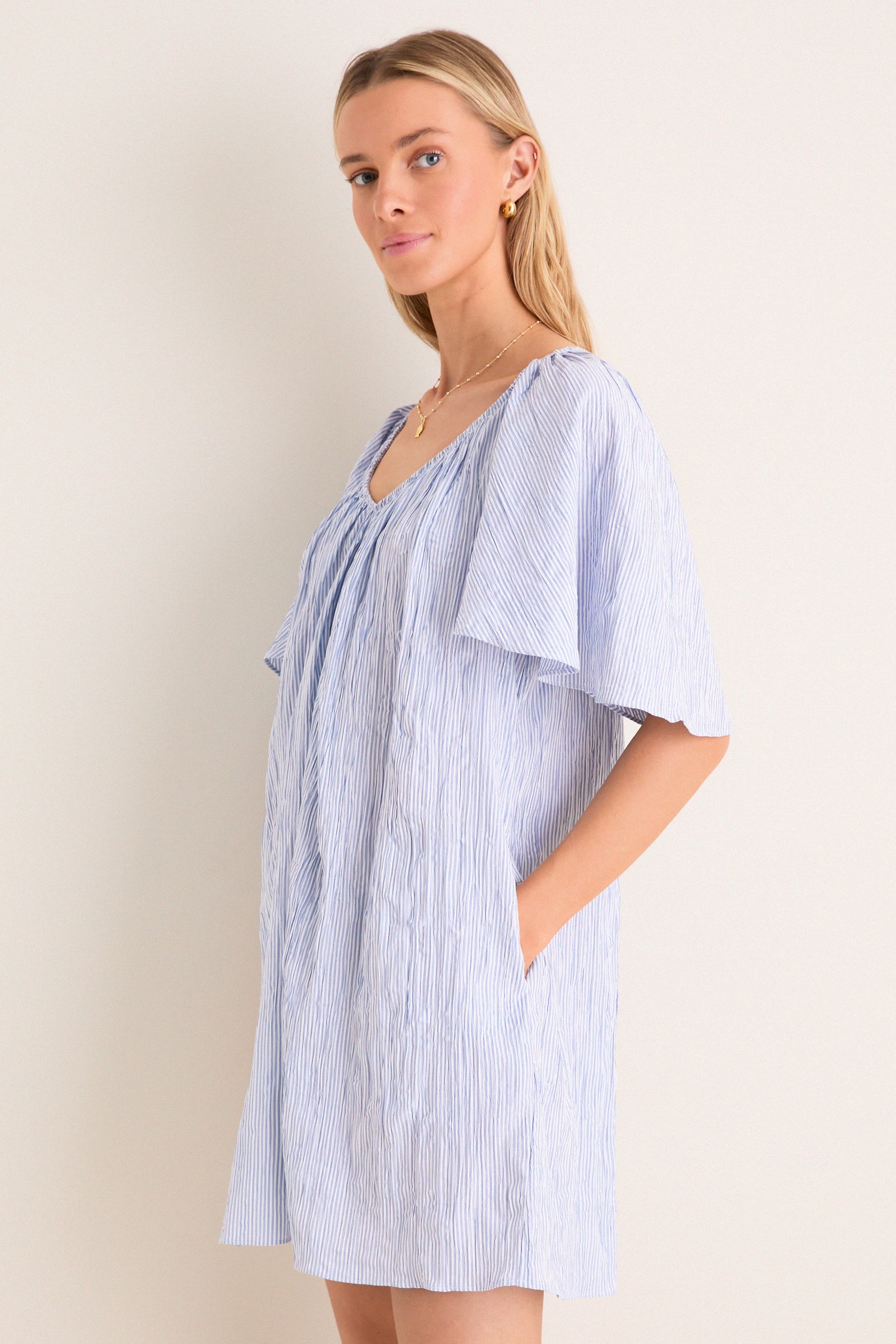 Young woman in a classic, effortless Saltwater Stripe Finn Dress with flutter sleeves and pockets, embodying a fun, high-end style suitable for any adventure.