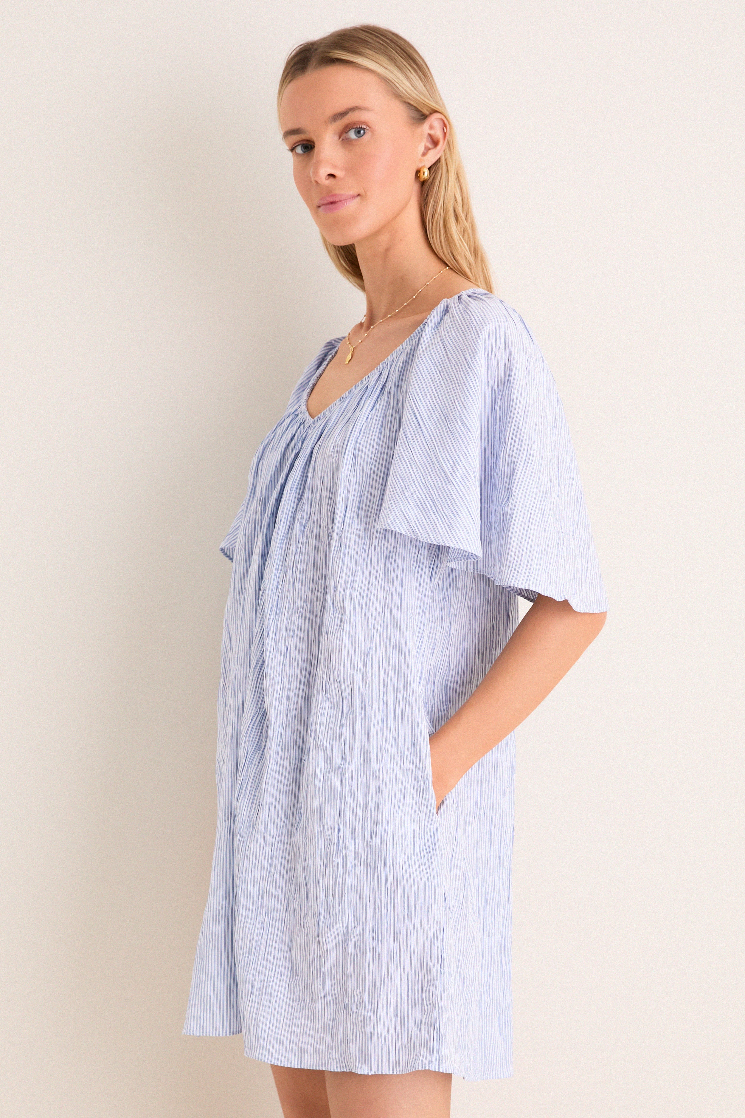 Young woman in a classic, effortless Saltwater Stripe Finn Dress with flutter sleeves and pockets, embodying a fun, high-end style suitable for any adventure.