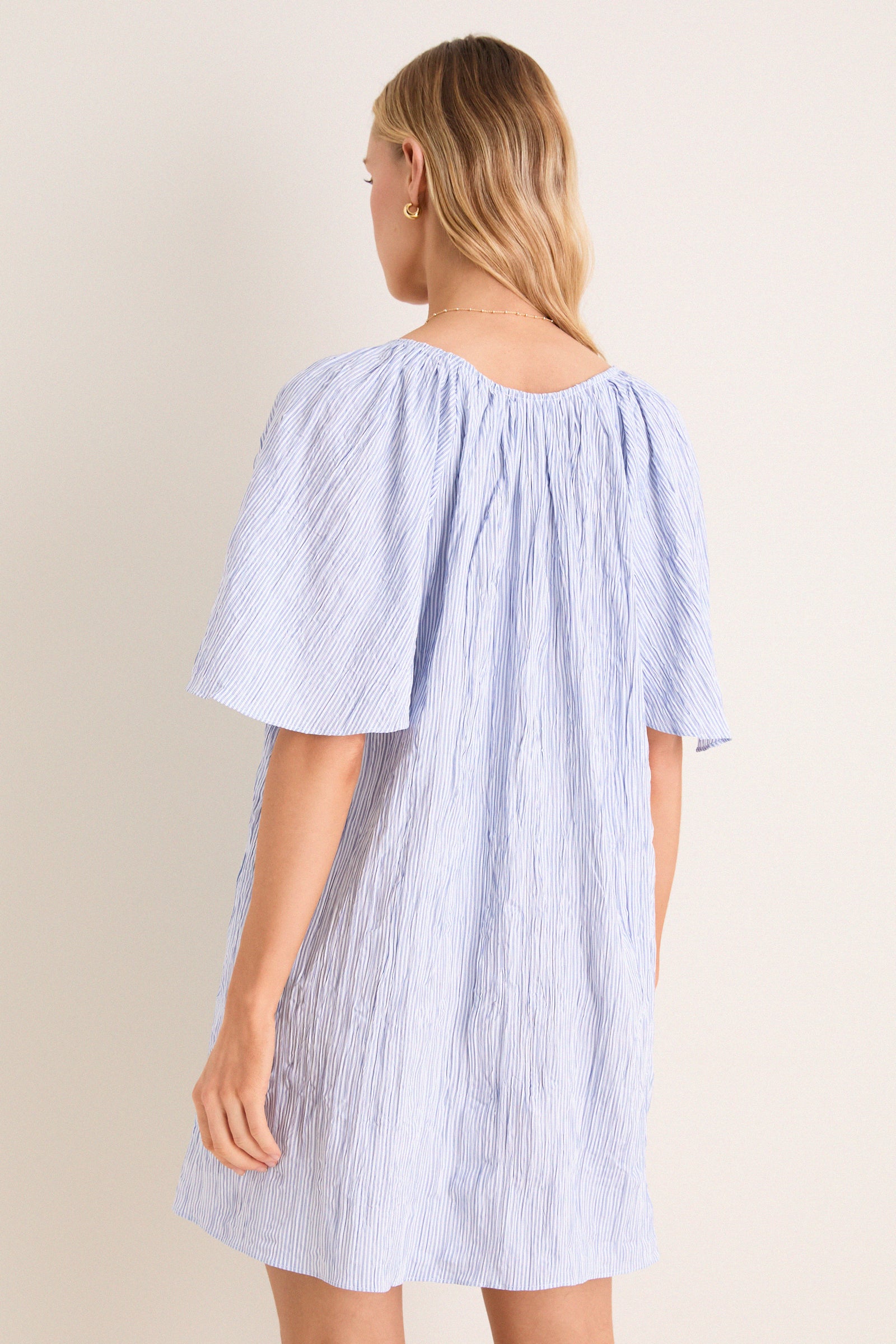 Back view of a woman in a classic, effortless Saltwater Stripe Finn Dress with a gathered V-neckline, showcasing high-end style and fun, flutter sleeves.
