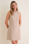 Young woman in a classic, sleeveless Mocha Gingham Yvette Mini Dress, smiling gently. The dress offers an effortless, high-end style perfect for fun, warm days.