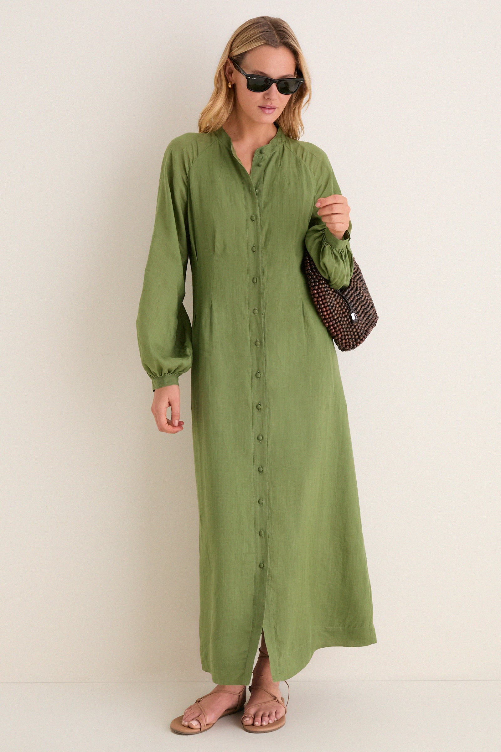 Woman wearing Cedar Green Button Down Granier Dress with sunglasses, holding a dark brown handbag. The classic, high-end dress features a relaxed fit and removable belt, paired with tan sandals.